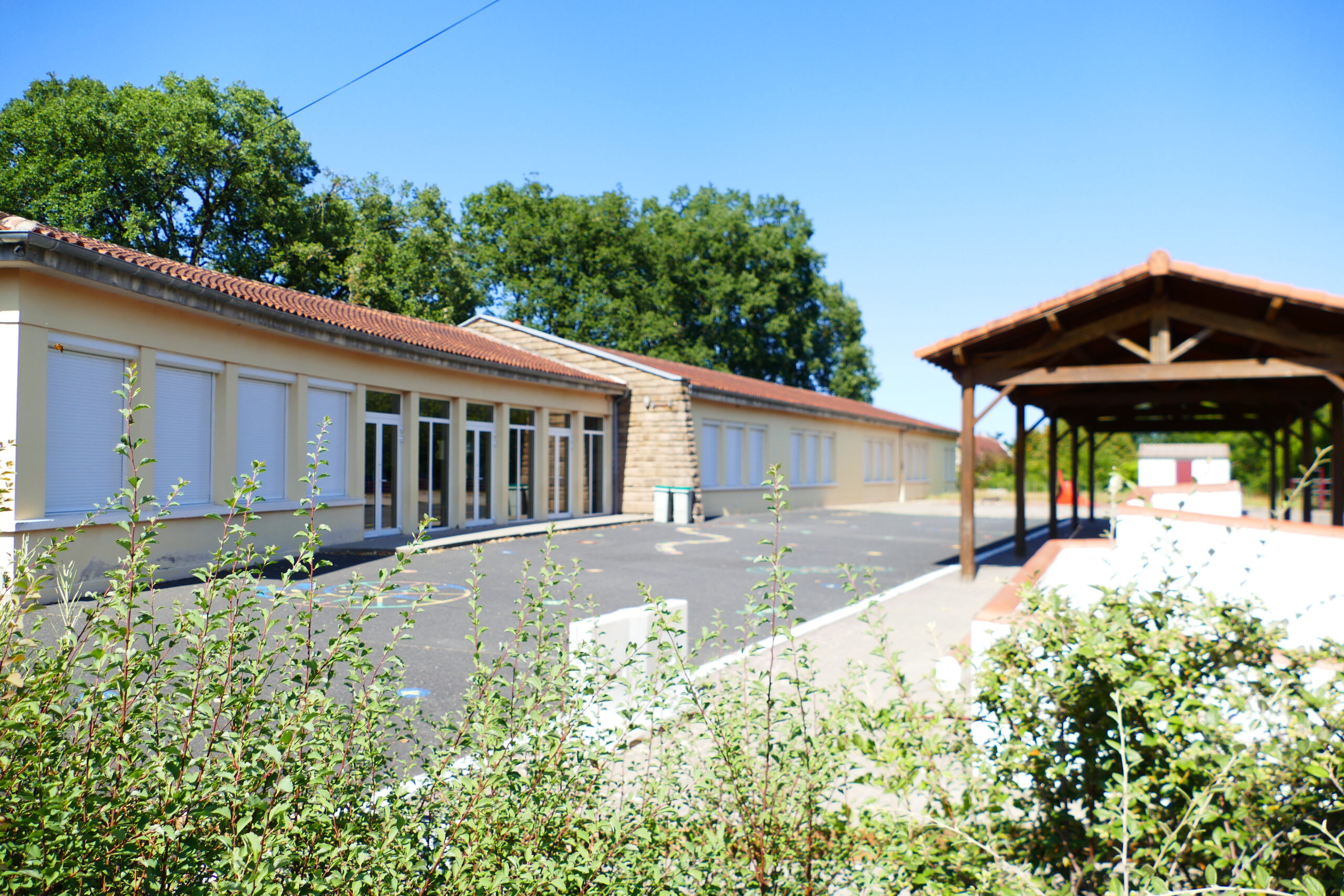 cour de l’école maternelle Photo de la cour de l'école maternelle dans laquelle se trouve un préau, des jeux dessinés au sol, un petit labyrinthe devant les salles de classe.